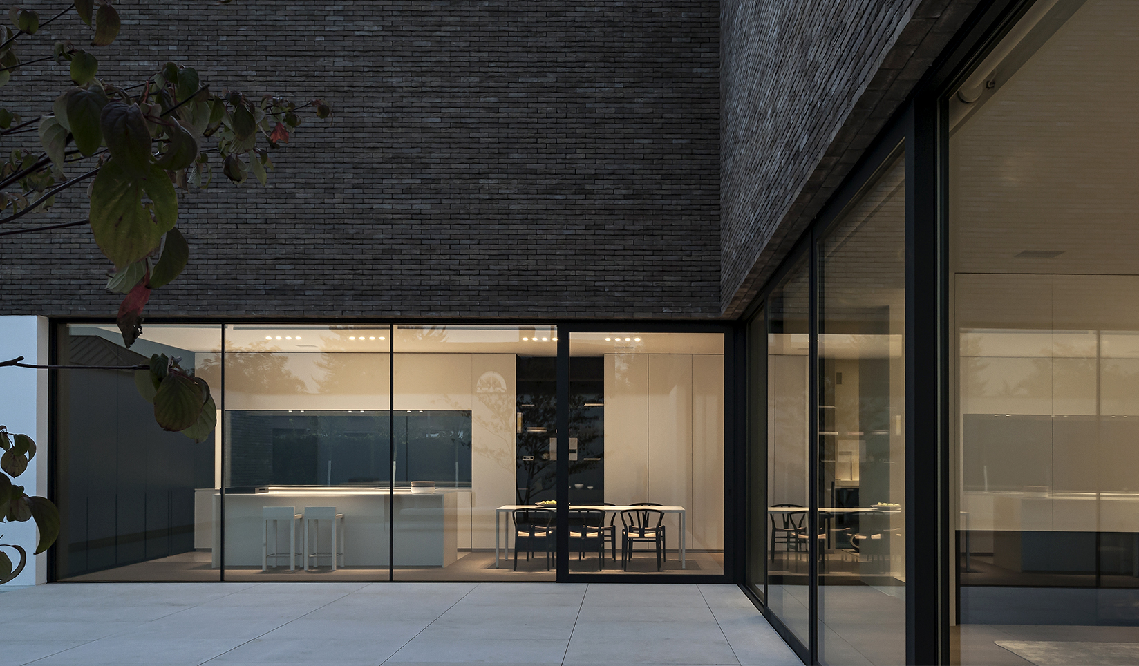 The brightly lit kitchen of a modern home shown through wall-to-wall windows at night.