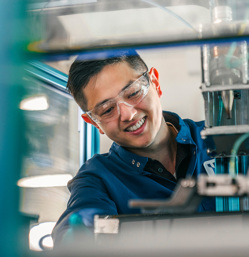 A Miru employee in safety glasses examines materials on a machine.