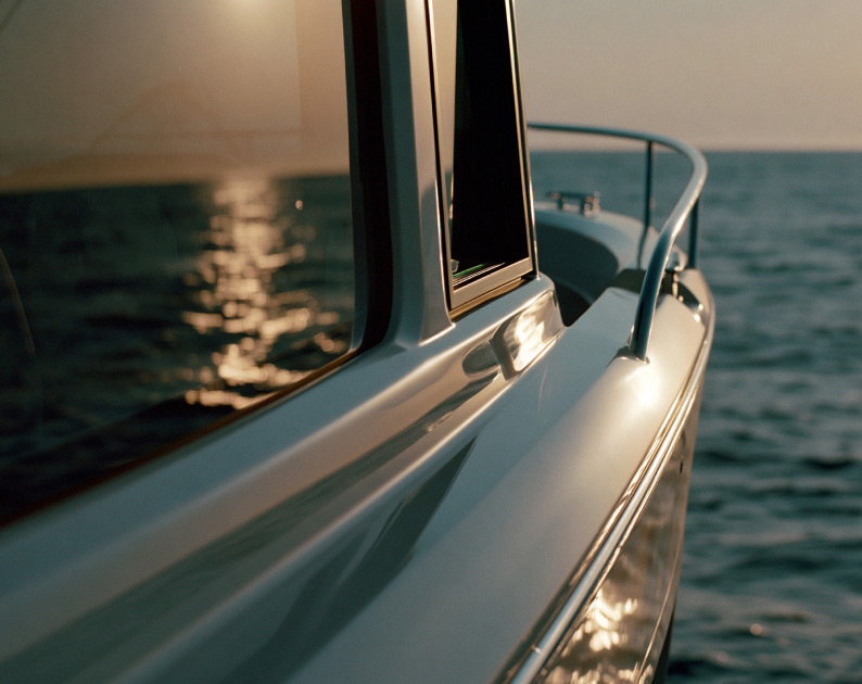 Close up of the windows on the side of a boat cabin reflecting the setting sun and water.